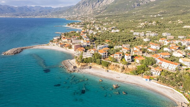 An aerial view of a coastal town with buildings along the shoreline, clear blue waters, and a rocky breakwater. - Avia Blue Maisonette - Steps From the Sea (West Mani)