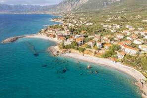 Vue aérienne d’une ville côtière, avec des bâtiments le long du littoral, une eau d’un bleu limpide et une digue rocheuse.