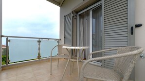 A balcony with wicker chairs and a small table, overlooking a body of water. - Avia Blue Maisonette - Steps From the Sea (West Mani)