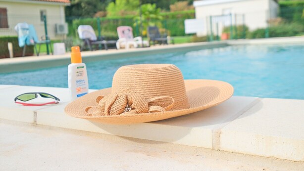 Área da piscina com chapéu, óculos de sol e frasco de protetor solar.
