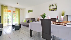 Uma área de refeições com uma mesa posta para dois, um sofá e uma televisão.