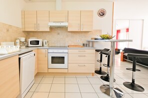 Une cuisine moderne avec des meubles de couleur bois clair, un four à micro-ondes, un four traditionnel et un petit coin repas équipé de tabourets.