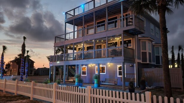A multi-story building with balconies, a white picket fence, and outdoor lighting.
