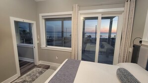 A bedroom with a bed, a window with curtains, a view of the outside, and a door leading to another room.