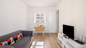 Un salon moderne avec un canapé gris, une table à manger en bois, un téléviseur et une porte blanche.