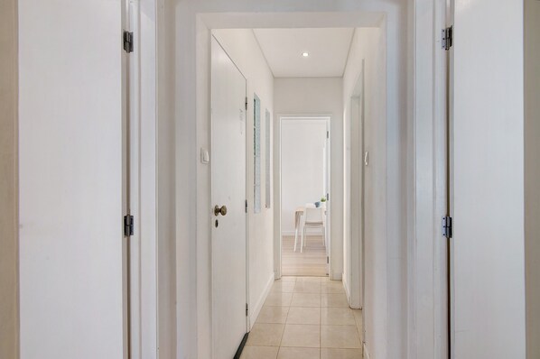 A hallway with white doors, a tiled floor, and a dining area with a table and chairs in the distance.