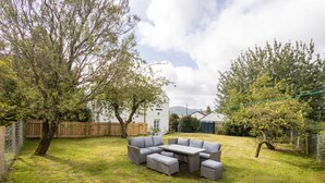 A backyard with a sectional sofa, a dining table, and a small garden area. - Host Stay Castle Hill Cottage (Keswick)