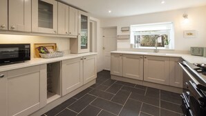 A modern kitchen with white cabinets, a black tiled floor, and a built-in microwave. - Host Stay Castle Hill Cottage (Keswick)