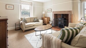 A living room with a fireplace, a sofa, a coffee table, and a lamp. - Host Stay Castle Hill Cottage (Keswick)