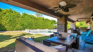 An outdoor patio with wicker furniture, a barbecue area, and a view of a lush green landscape. - Beautiful and Private 4 Bedroom Private Pool Home (Bermuda Dunes)