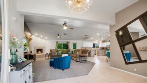 A spacious living room with a fireplace, a blue sofa, and a dining area with a kitchen in the background. - Beautiful and Private 4 Bedroom Private Pool Home (Bermuda Dunes)