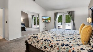 A bedroom with a large bed, a TV, a ceiling fan, and a view of a pool through the glass doors. - Beautiful and Private 4 Bedroom Private Pool Home (Bermuda Dunes)