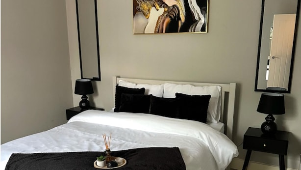 A neatly made bed with white linens, black pillows, and a black throw blanket. There are two bedside tables with lamps, and a painting hangs above the bed. - City Chic Retreat In Birmingham (Birmingham)