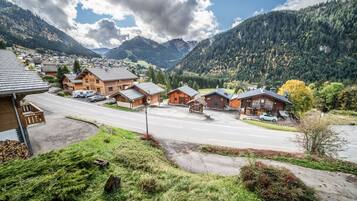 A mountain village with traditional wooden houses, a main road, and a view of the surrounding forested mountains.
