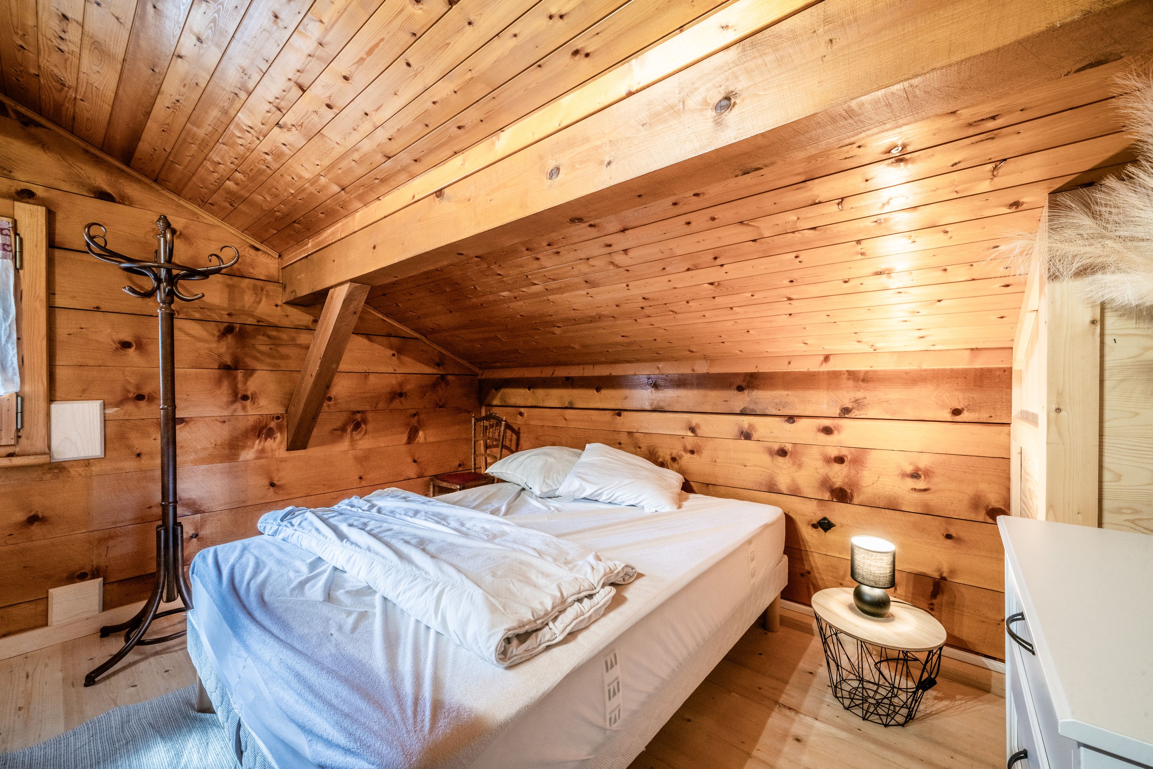 Une chambre à coucher chaleureuse, avec des murs en bois, comprenant un lit, une table de chevet, une chaise et une lampe sur pied.