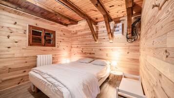 A wooden cabin room with a bed, a nightstand, and a window.