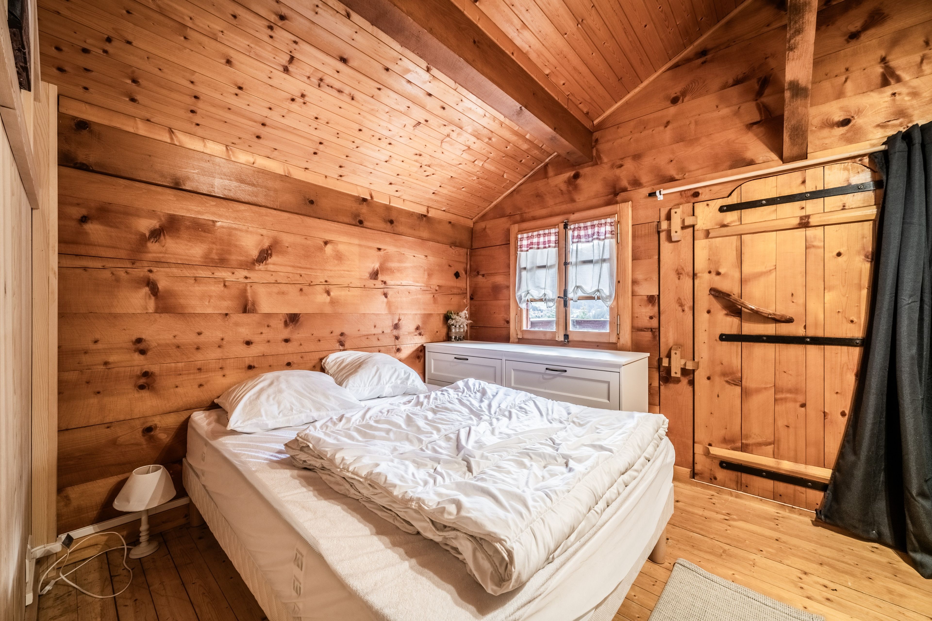 Ein Schlafzimmer einer Holzhütte mit einem Bett, einem Schminktisch und einem Fenster mit Vorhängen.