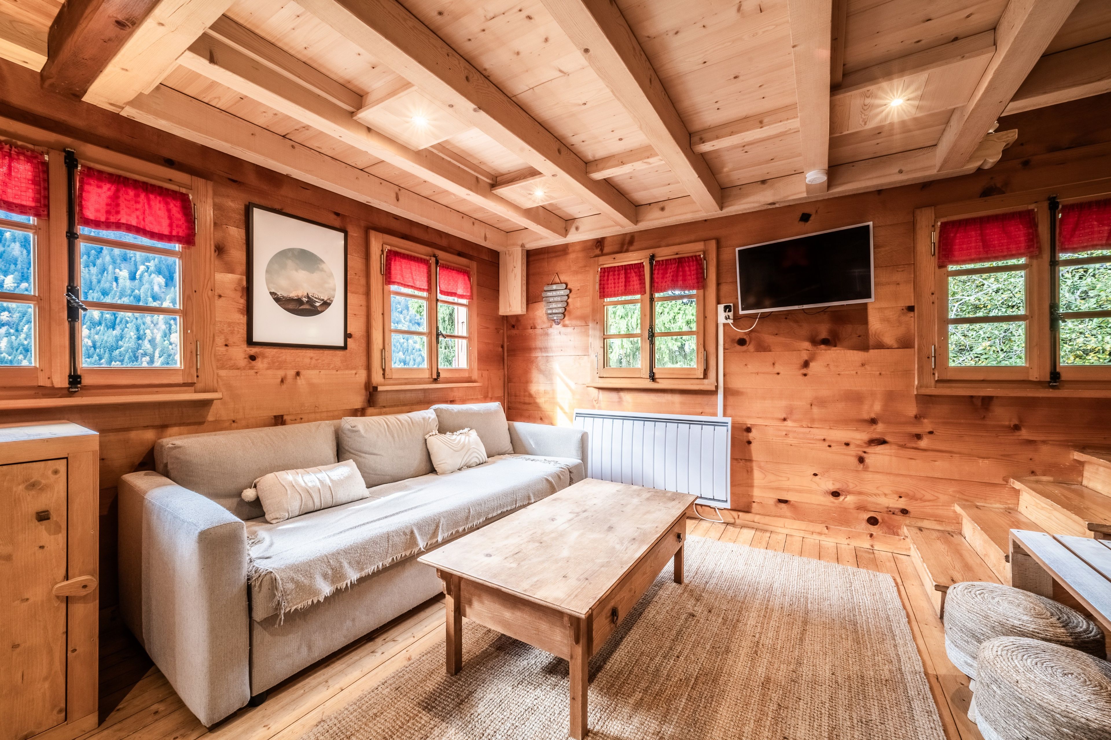 A wooden interior with a sofa, a table, and a TV mounted on the wall.