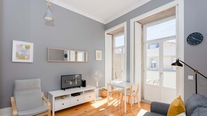 A modern living room with a grey sofa, a white TV stand, a dining table with chairs, and a large window with a view. - Liiiving in Porto - Silver Light Apartment (Porto)