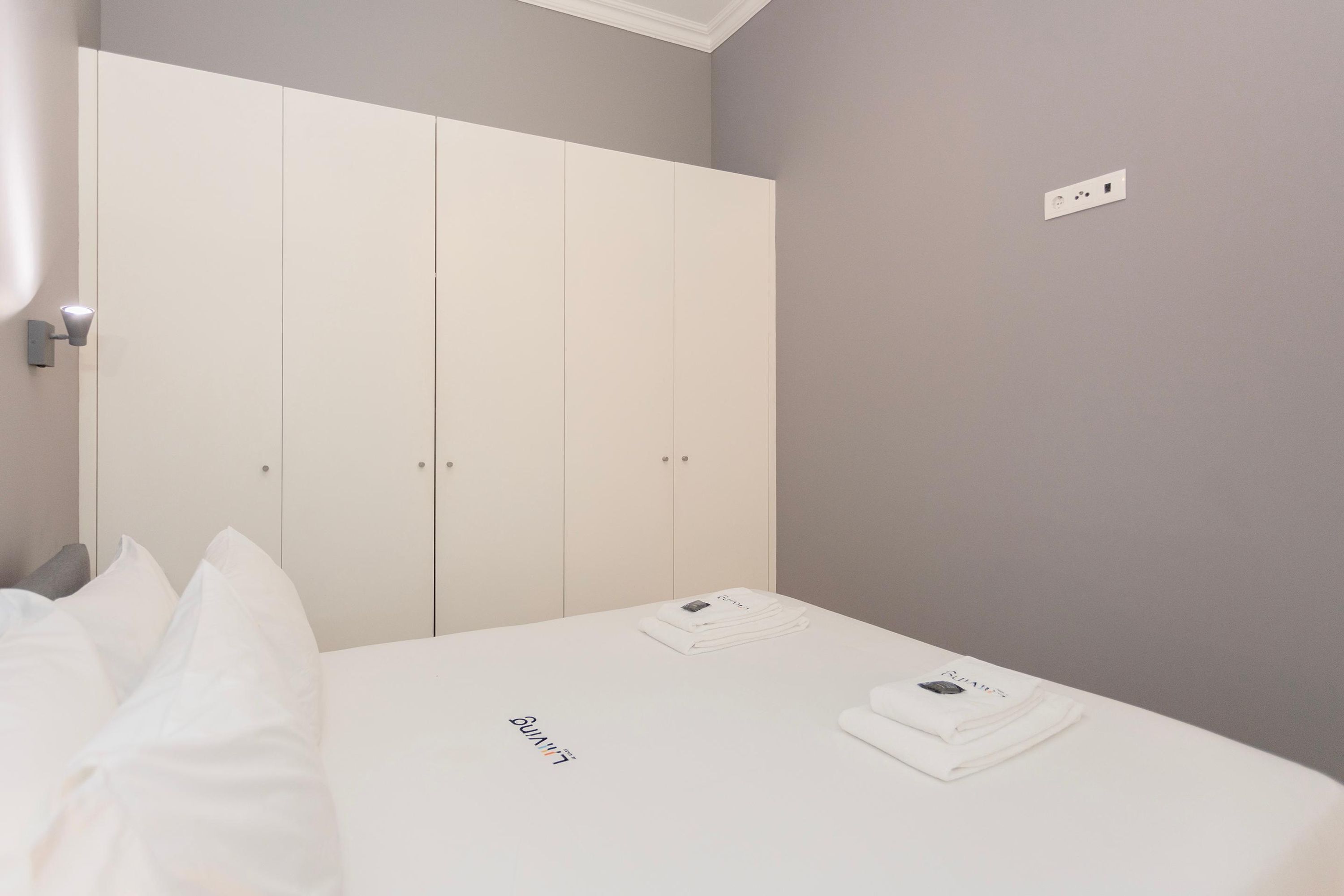 A bedroom with a bed, white bedding, a wardrobe, and a small table with items on it.