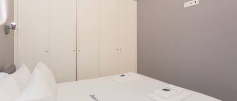 A bedroom with a bed, white bedding, a wardrobe, and a small table with items on it.