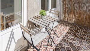 A balcony with a patterned floor, a wooden chair, a small plant, and a bamboo screen. - Liiiving in Porto - Silver Light Apartment (Porto)