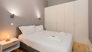 A neatly made bed with white linens, a bedside table with a lamp, and a wardrobe with sliding doors. - Liiiving in Porto - Silver Light Apartment (Porto)