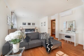 Un salon moderne avec un canapé d’angle gris, une table basse en verre et un bureau blanc avec une chaise.