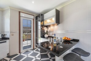 Une cuisine moderne avec un plan de travail noir, des armoires blanches et une porte vitrée donnant sur un balcon.