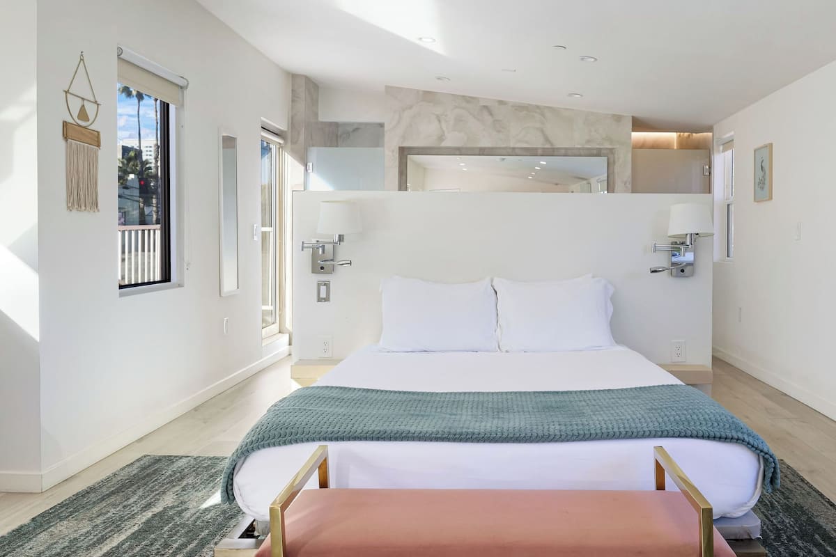 Un dormitorio moderno con una cama grande, lámparas de noche, una ventana con vistas y un banco al pie de la cama.