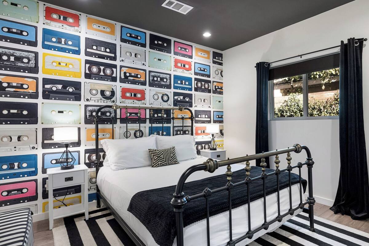 Un dormitorio con cama, mesita de noche, cómoda y una pared cubierta de cintas de cassette.