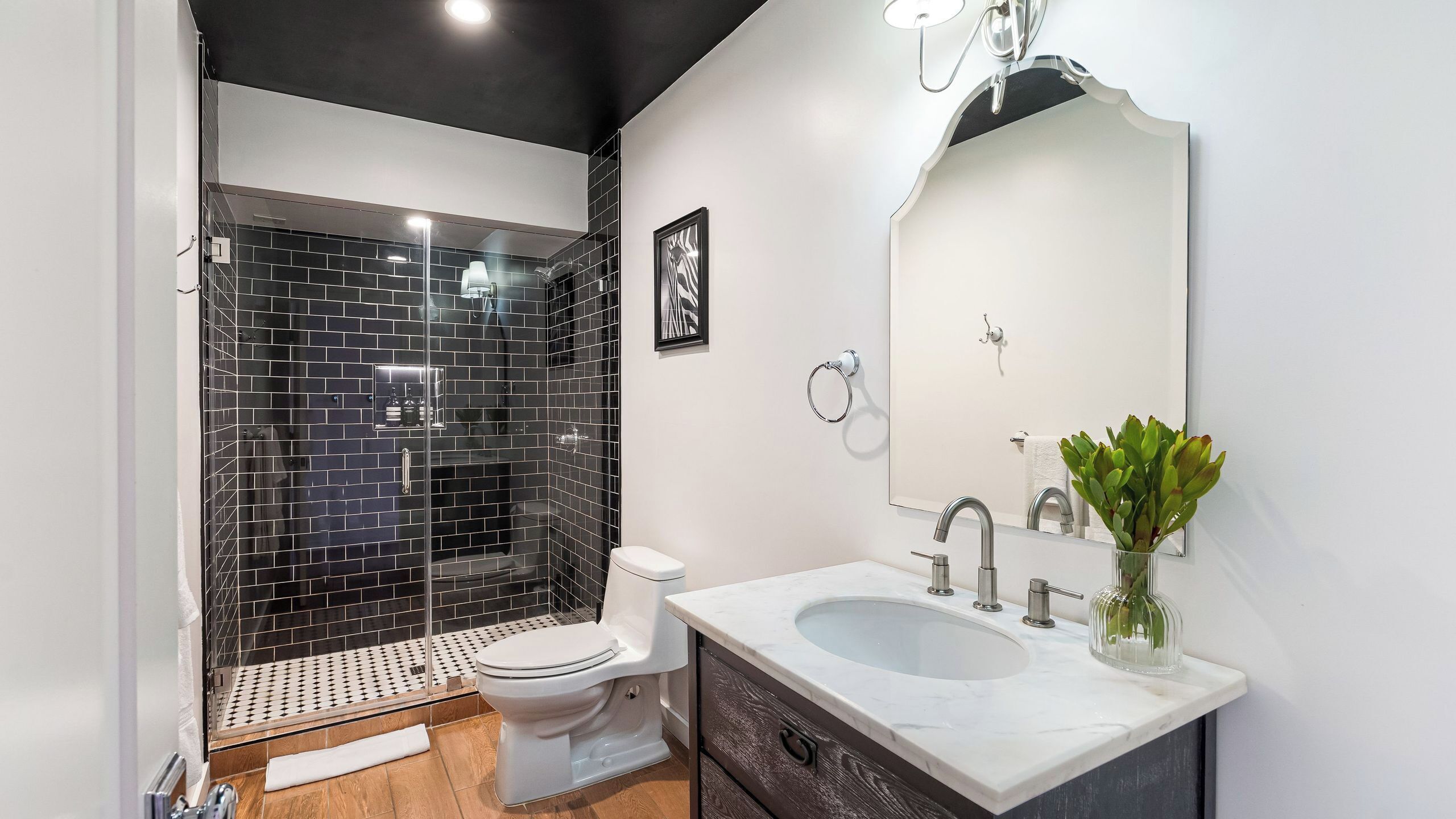 Un baño moderno con ducha envuelta en vidrio, inodoro blanco, lavamanos de mármol y un espejo.