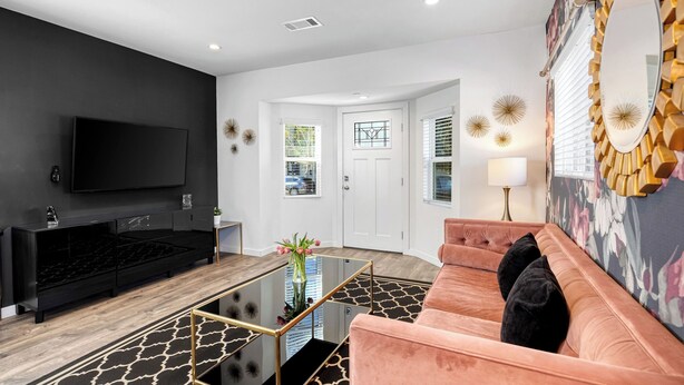 Uma sala de estar moderna com um rack preto, um sofá rosa e uma mesa de centro de vidro.