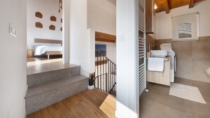 Een modern interieur met een trap naar een slaapkamer, een badkamer met een wastafel en handdoekhouder, en uitzicht op het landschap door een raam.