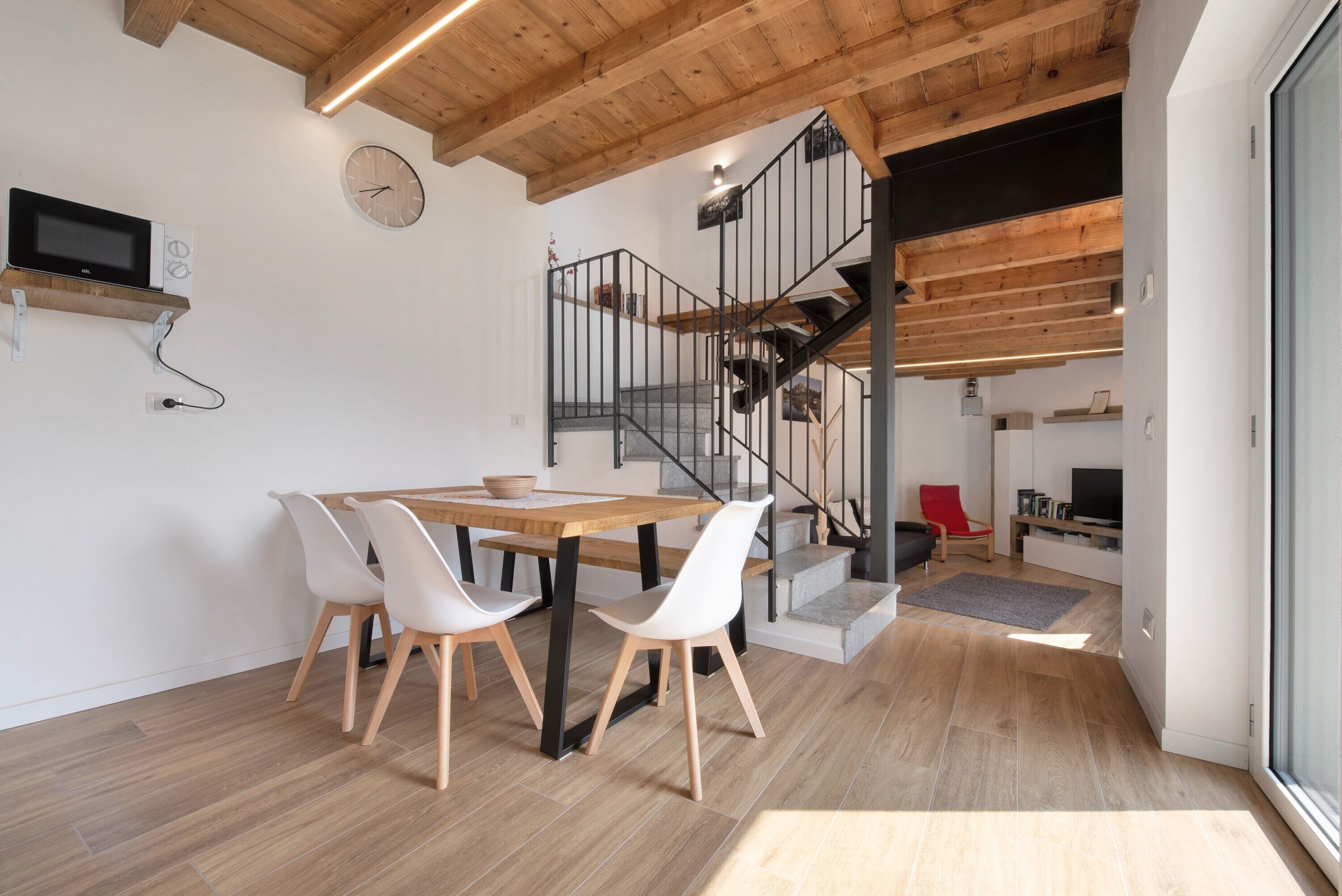 Une cuisine moderne avec une table et des chaises en bois, un four à micro-ondes encastré et un escalier menant à un niveau supérieur.