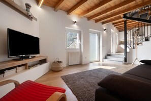 Un salon moderne doté d’un téléviseur à écran plat, de poutres en bois, d’un escalier et offrant une vue sur l’extérieur.