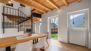 Een eetruimte met een houten tafel, witte stoelen, een trap en uitzicht door een glazen deur.