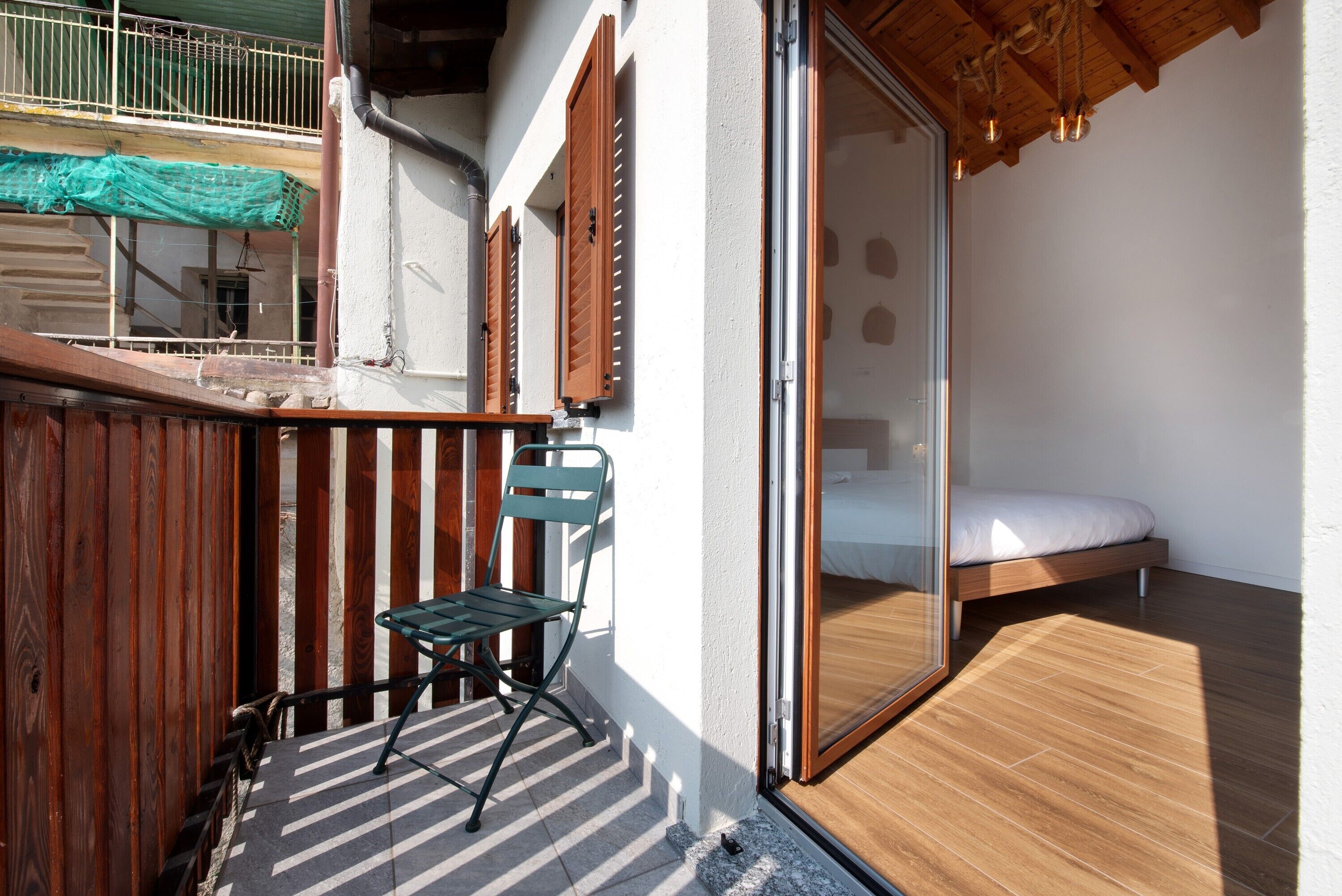 Een balkon met een houten vloer, een groene stoel en een bed met een witte matras.