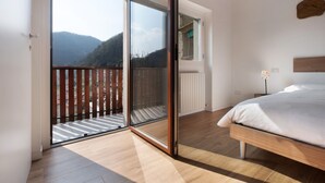 Een slaapkamer met een grote schuifdeur die leidt naar een balkon, een houten bed en uitzicht op een bergachtig landschap.