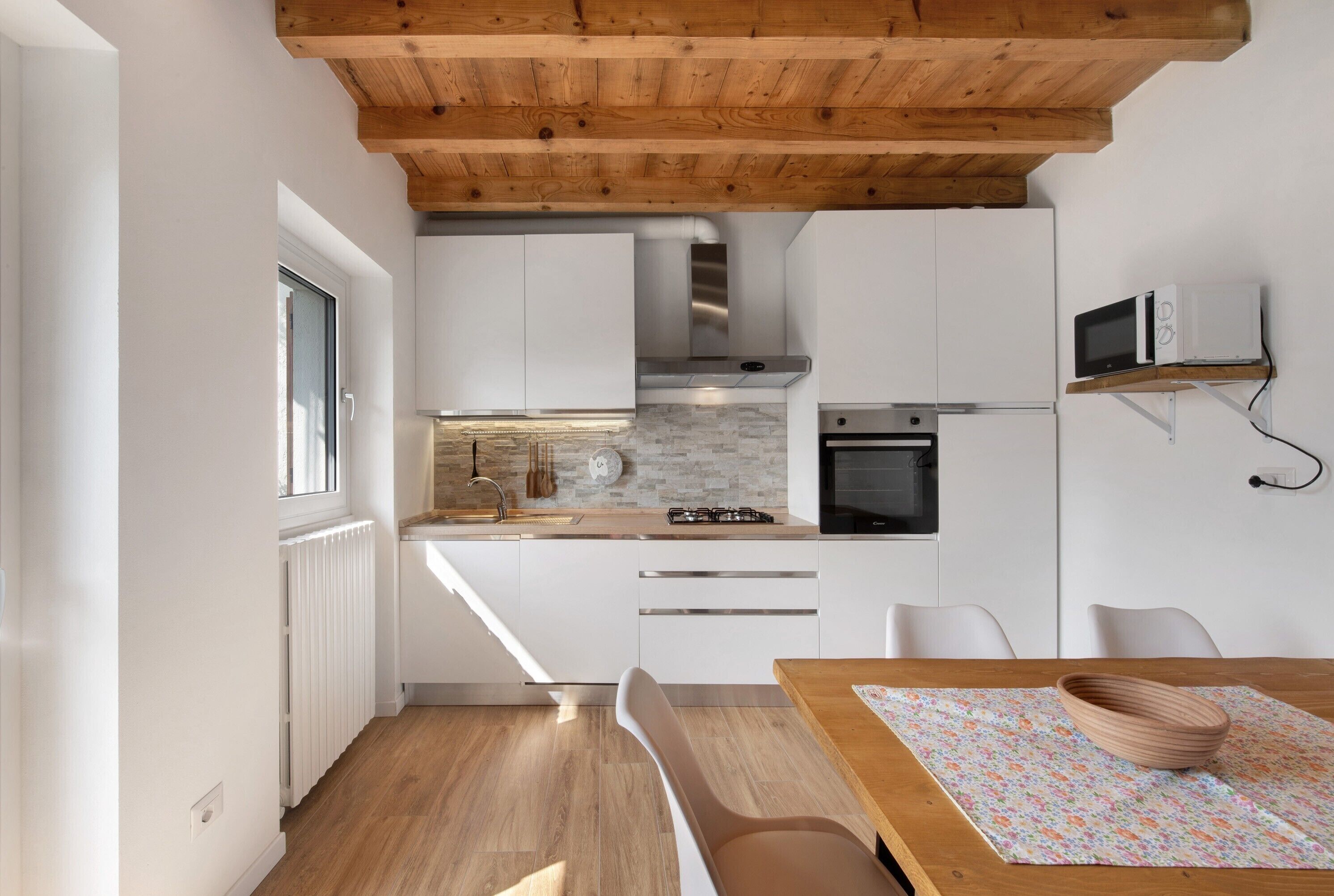 A modern kitchen with white cabinets, a wooden ceiling, and a dining area with a table and chairs.