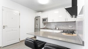 Una cocina moderna con armarios blancos, un refrigerador de acero inoxidable, un microondas y una estufa a gas. Hay dos taburetes negros en la isla de la cocina.