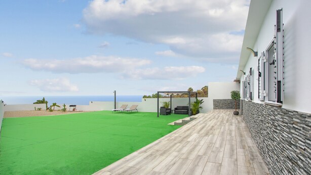 Una terraza en la azotea con césped, zona de estar y vistas al océano.