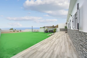 Una terraza en la azotea con césped, zona de estar y vistas al océano.