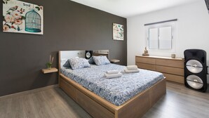 Un dormitorio con cama, mesitas de noche, cómoda, ventana y decoración en la pared.