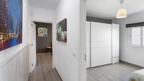 Un pasillo con una puerta que da a un dormitorio, un cuadro de una jaula de pájaros y una lámpara en el techo.