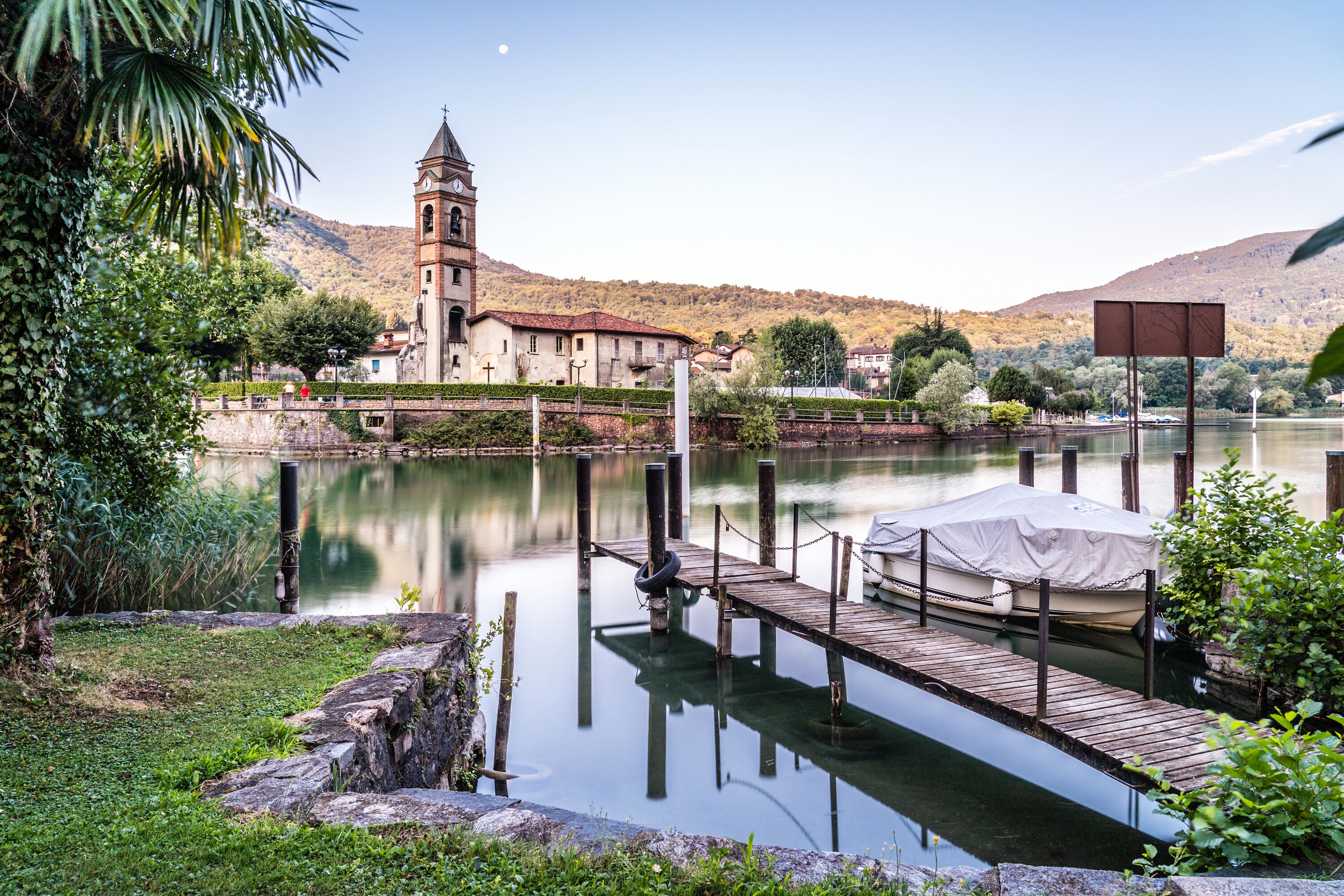 Una escena tranquila junto al lago, con una iglesia, un muelle de madera y un bote cubierto con una lona.