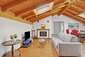 A high-ceilinged room with a fireplace, a sofa, a television, and a dining area with chairs. - Attico a Caslano (Caslano)