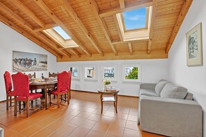 A dining area with a wooden ceiling, red upholstered chairs, a round table, and a grey sofa. - Attico a Caslano (Caslano)