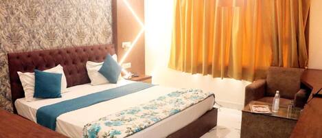 A hotel room with a large bed, a sofa, a small table, and a curtain.