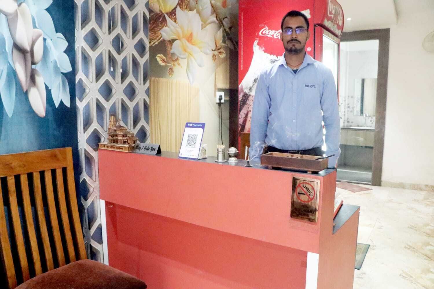 Mostrador de recepción de hotel con un anuncio de Coca-Cola al fondo, un código QR para pagos y un cartel de prohibición de fumar.